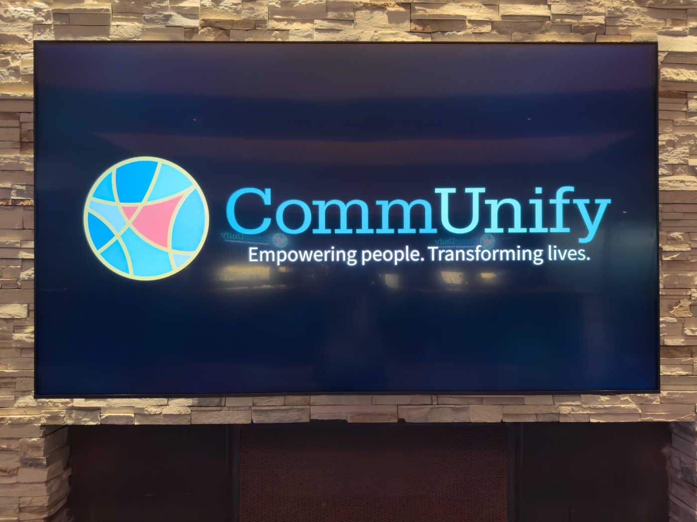 The CommUnify mission on the ballroom screen — Empowering people. Transforming lives.